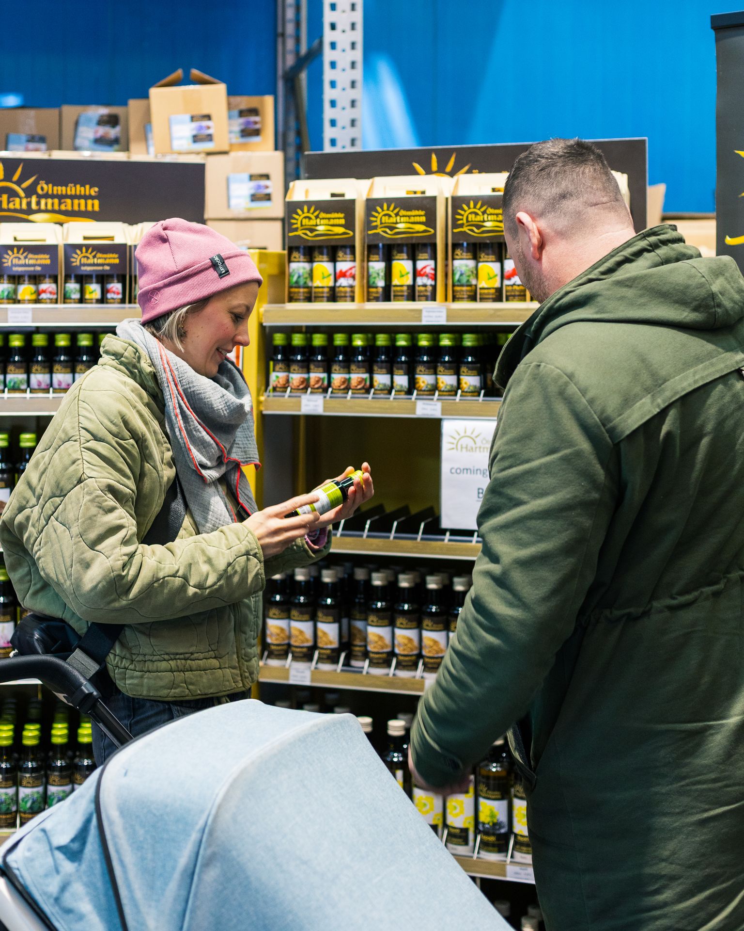 Besuchen Sie uns vor Ort und entdecken Sie unsere Produktvielfalt Kunden betrachten eine Flasche Öl im Verkaufsregal während des Werksverkaufs der Ölmühle Hartmann in Biburg.
